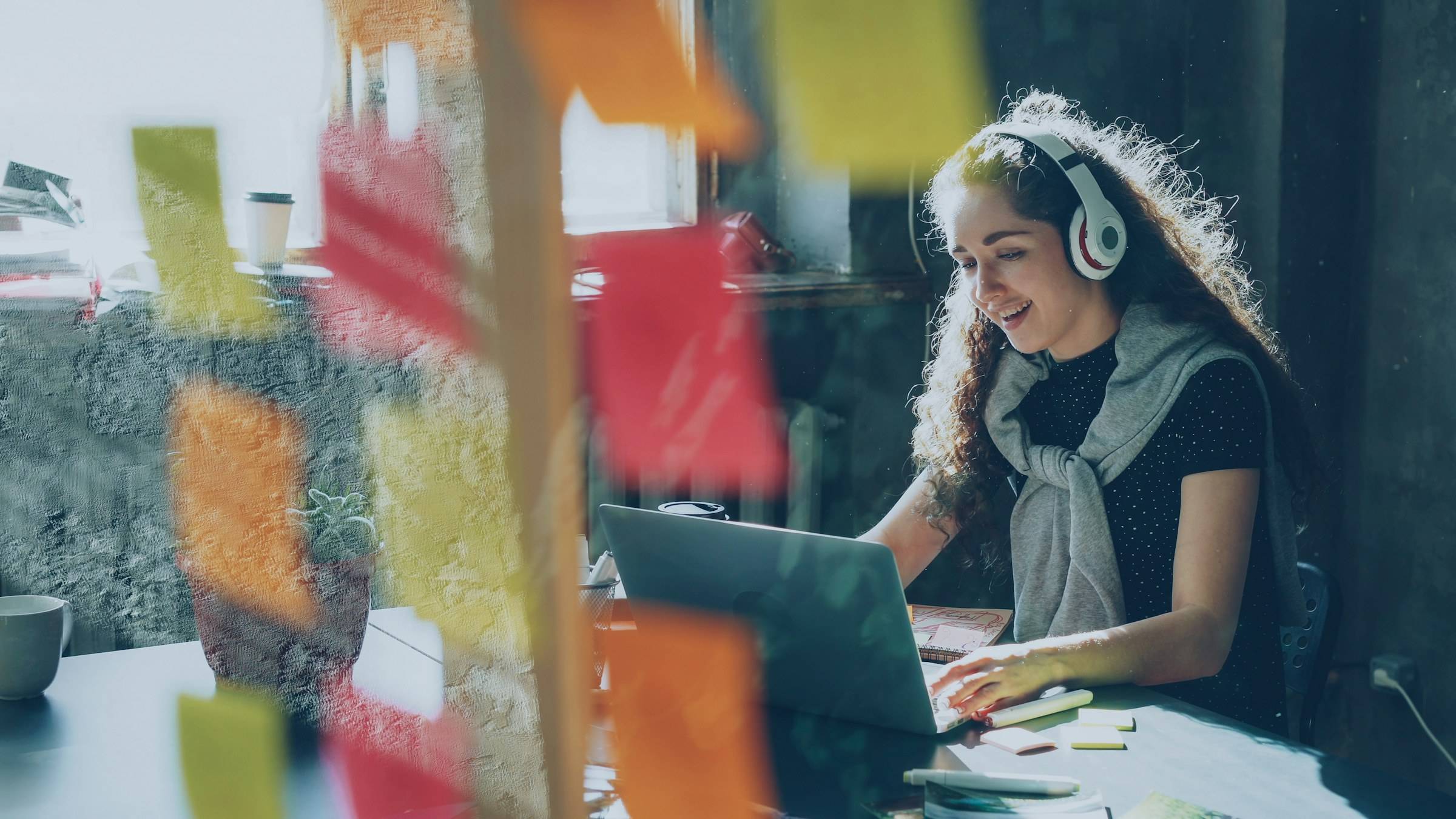 A young woman with headphones works on her laptop